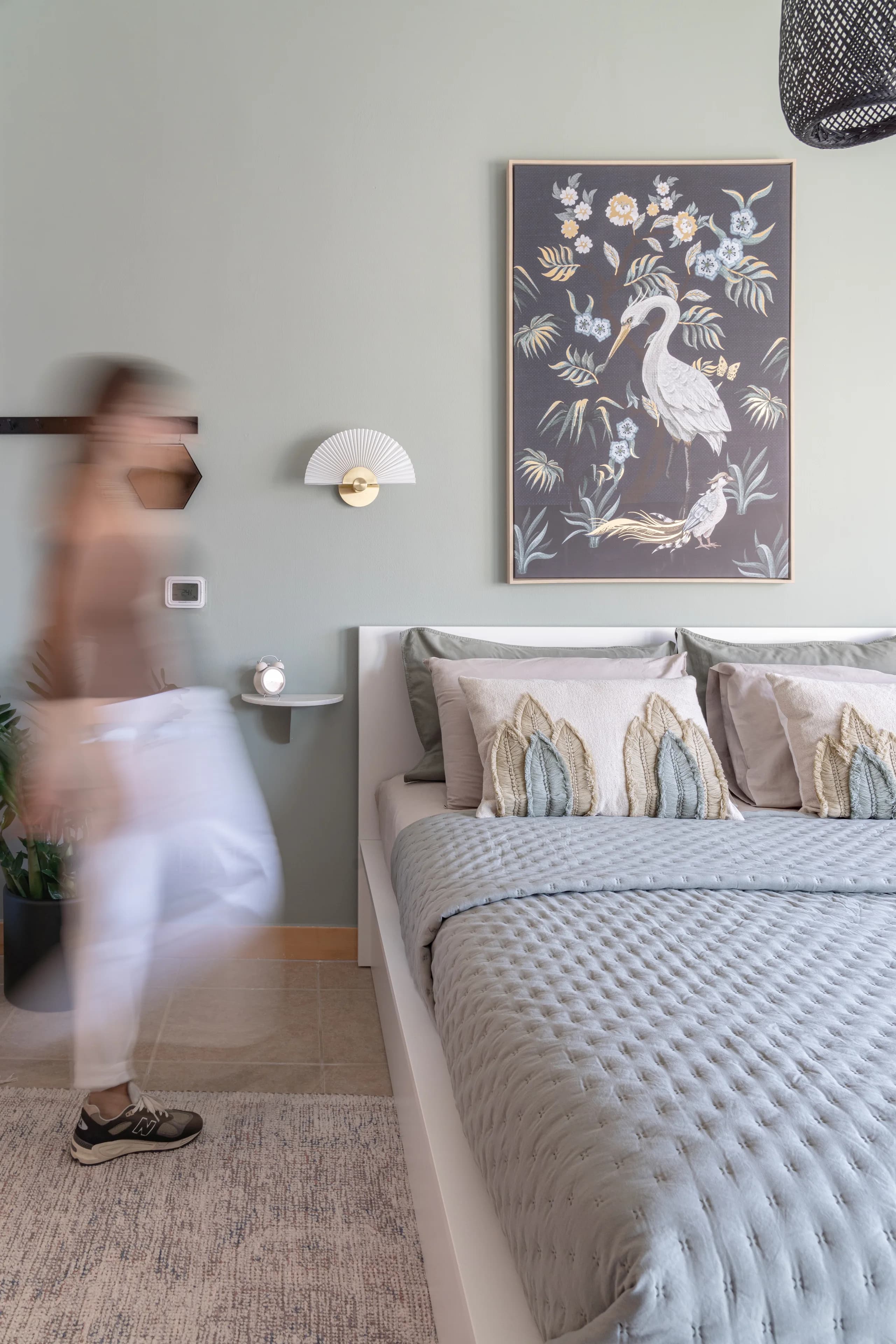 Bedroom in soft sage with a framed heron artwork and layered textile cushions