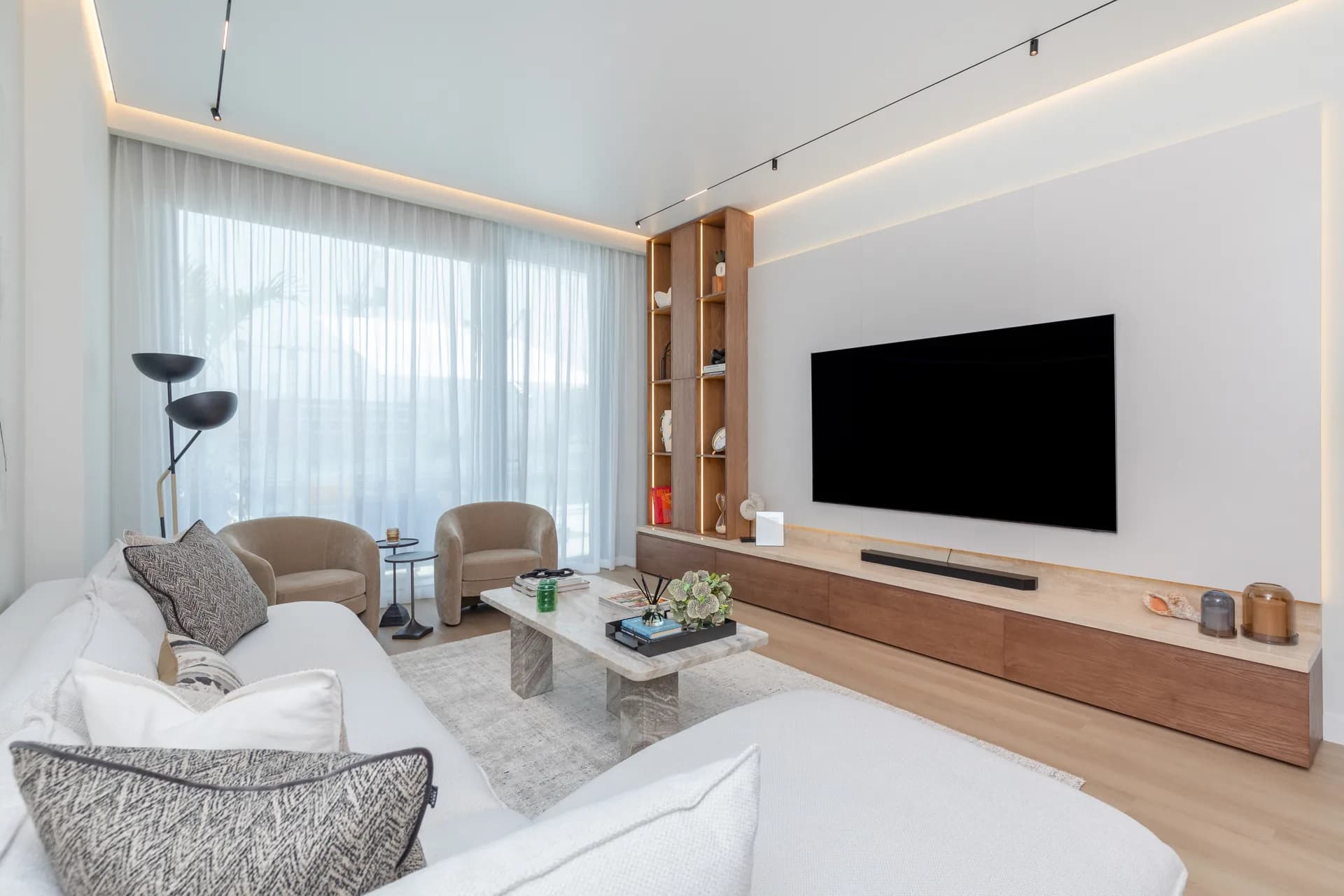 Living room with full-width walnut media wall, curved armchairs and city view