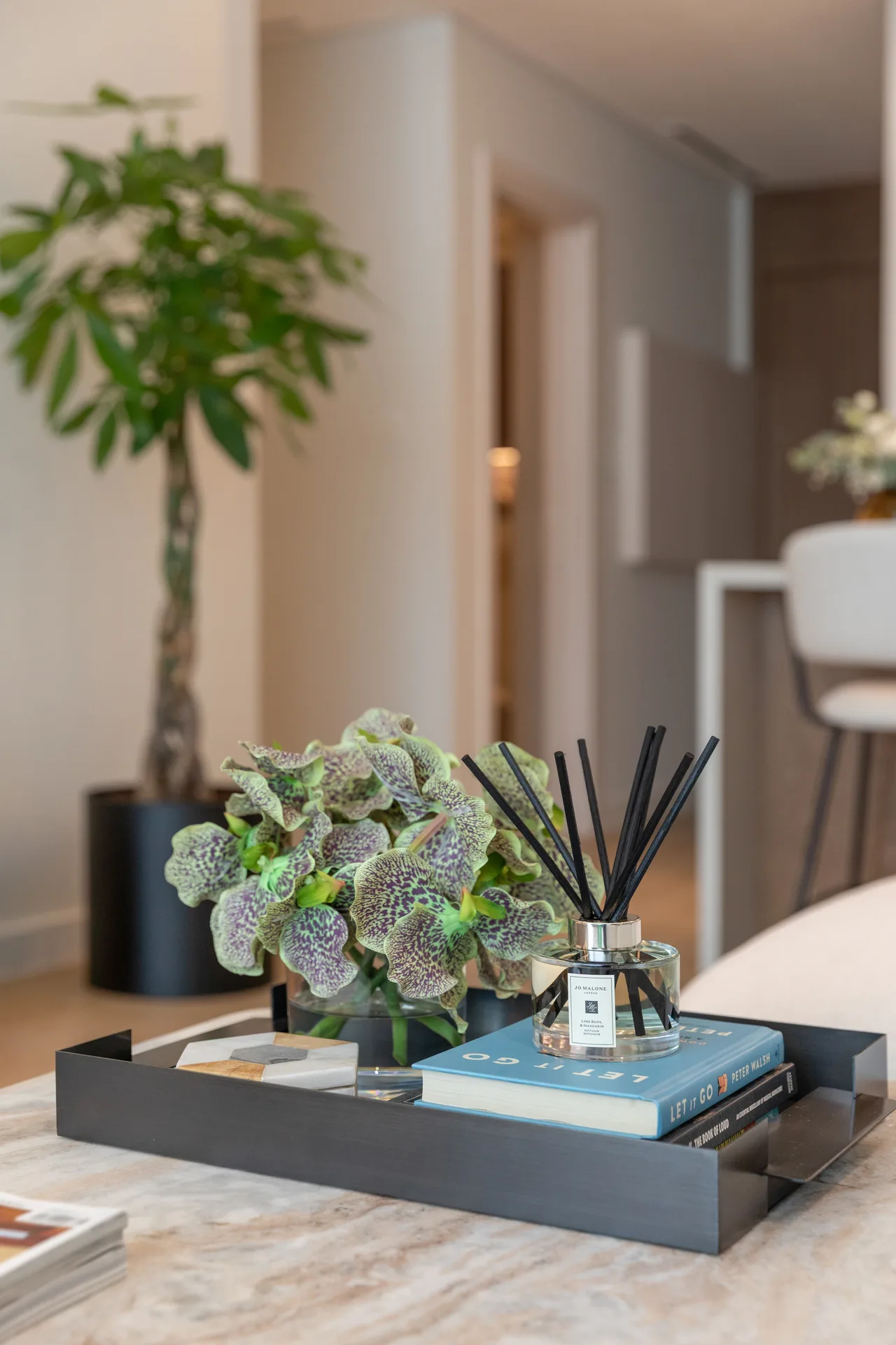 Styling detail — orchids and a scent diffuser on a dark tray over marble